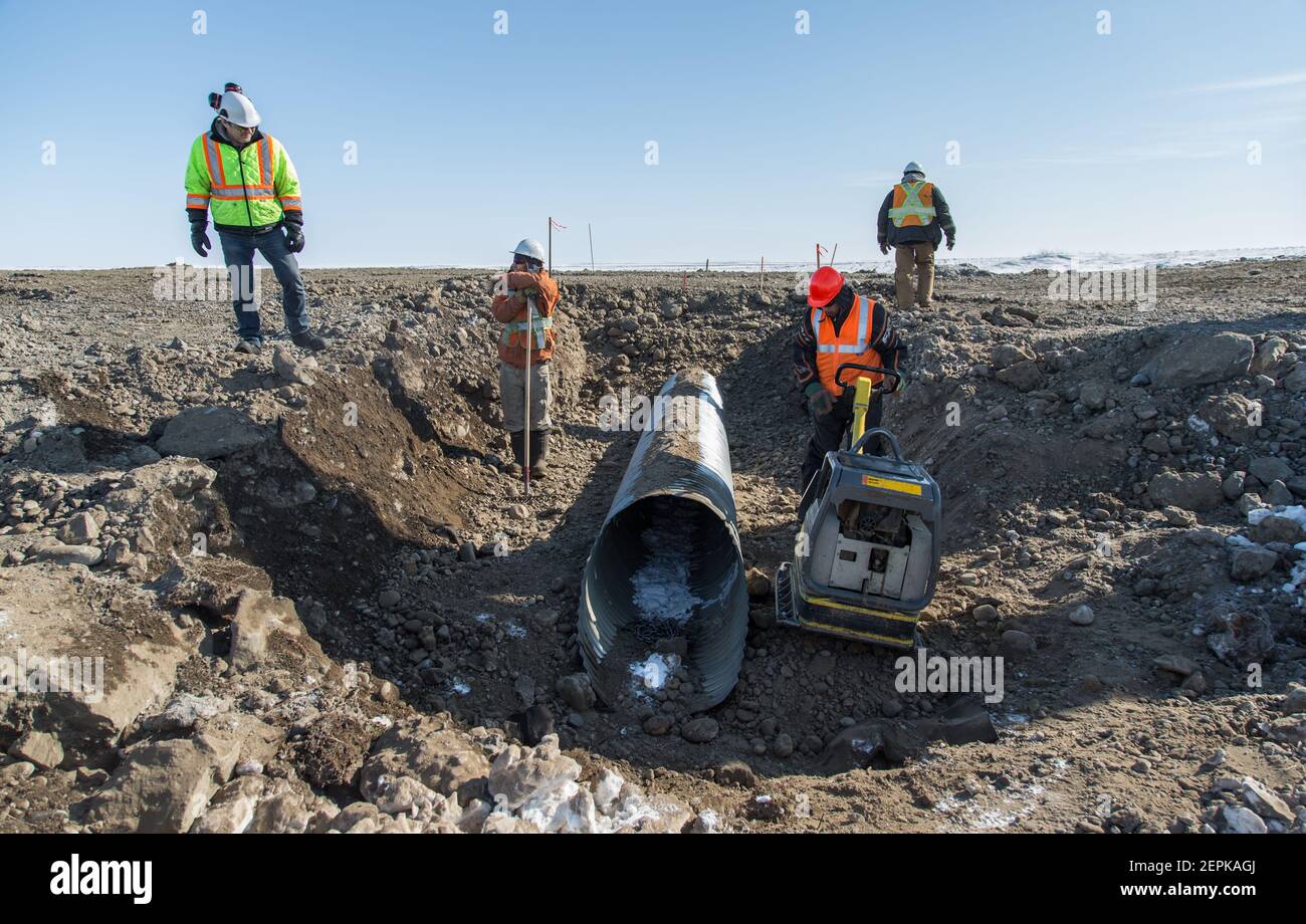 Quattro lavoratori maschi indigeni che installano il culvert durante la costruzione invernale dell'autostrada Inuvik-Tuktoyaktuk, territori del Nord-Ovest, artico del Canada. Foto Stock