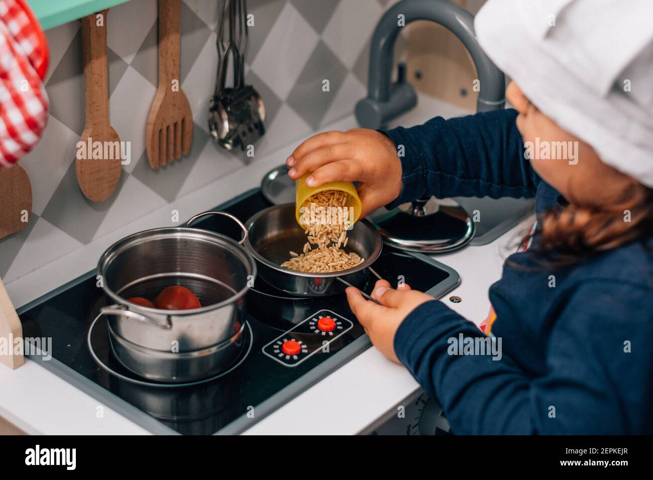 Bambina caucasica, indossando un cappello da chef, giocando ad essere una cuoca nella sua piccola cucina giocattolo. Foto Stock