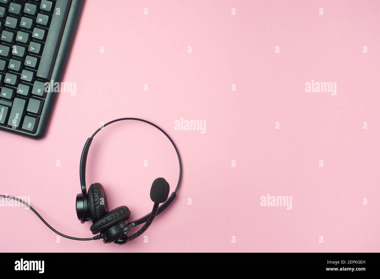 Scrivania da ufficio minima. Piatto - tastiera e auricolari neri su sfondo rosa. Vista dall'alto. Concetto di ambiente di lavoro. Foto Stock