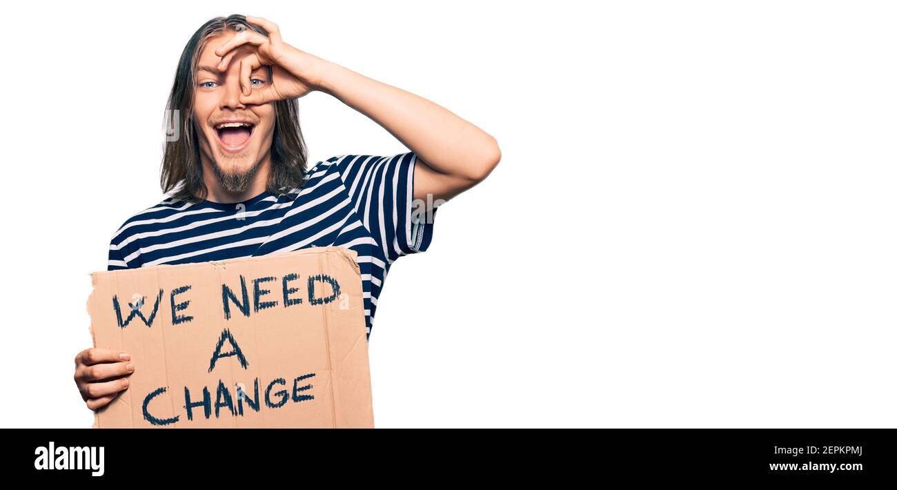 Bell'uomo caucasico con i capelli lunghi che tengono abbiamo bisogno di un cambia banner sorridente felice facendo ok segno con mano sopra occhio che guarda attraverso le dita Foto Stock