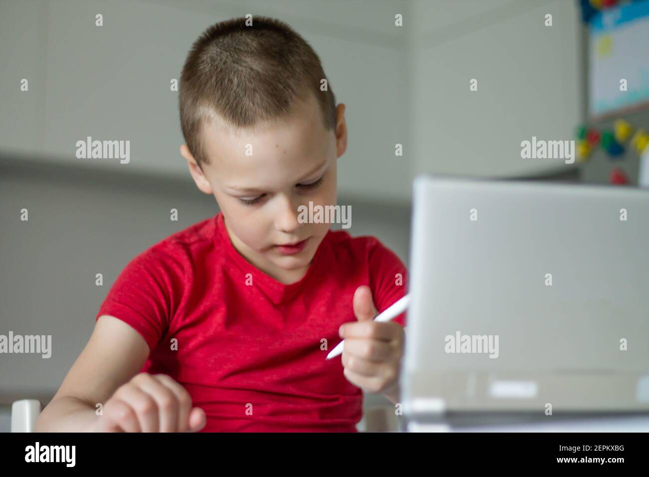 Boy 6-10 completa le lezioni scolastiche e i compiti online in cucina, guardando il computer tablet. Il concetto di istruzione a distanza. Rimani a casa. Foto Stock