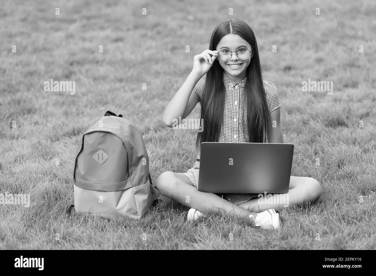 la ragazza teenager usa il computer sull'erba verde nel parco. bambino con zaino e notebook. nuova tecnologia nella vita moderna. studio. bambino felice in occhiali che lavora su laptop. formazione online. ritorno a scuola. Foto Stock