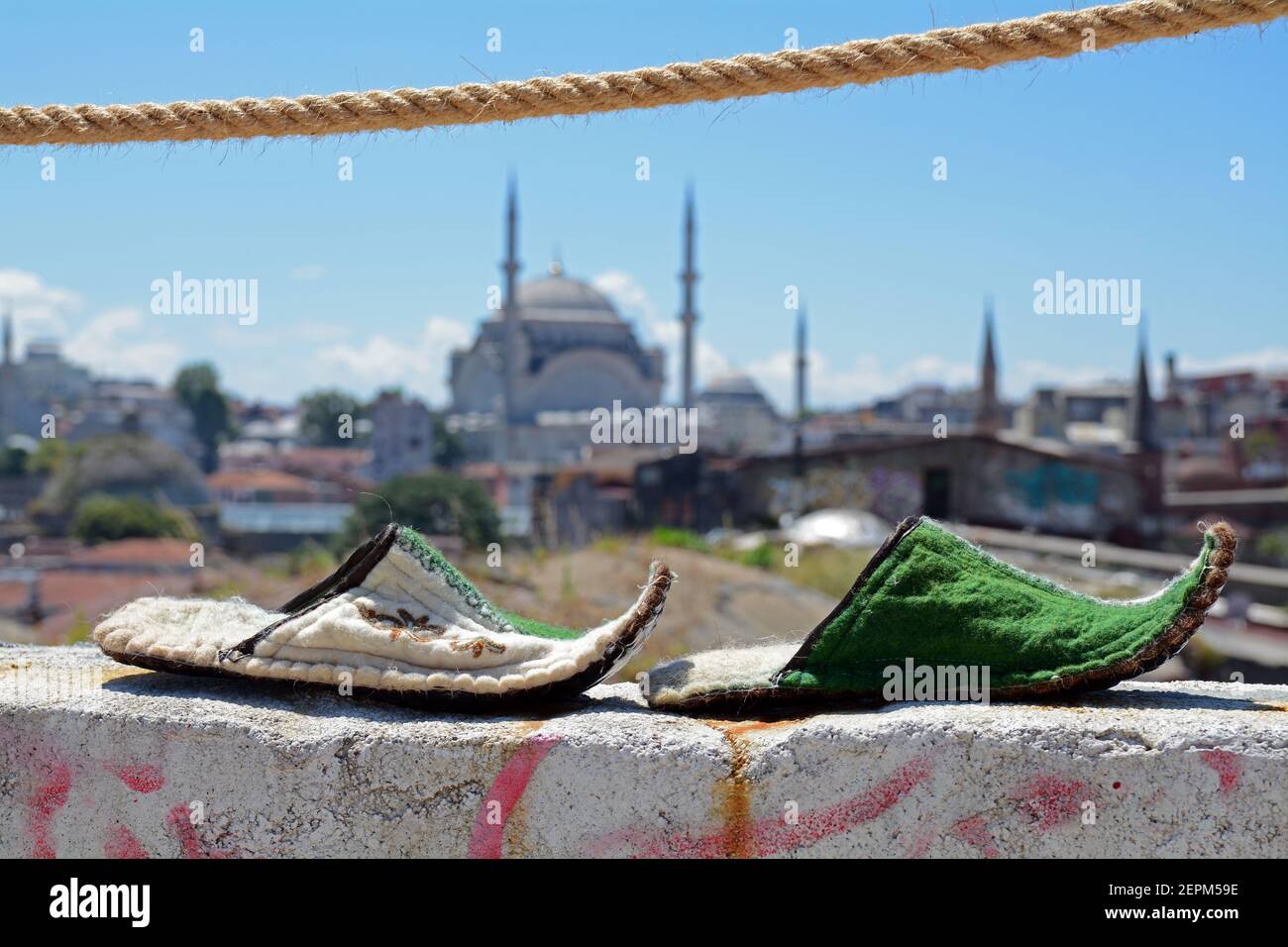 Un paio di scarpe tradizionali arabe che si asciugano su un muro a Istanbul con la città e la moschea sullo sfondo. Foto Stock