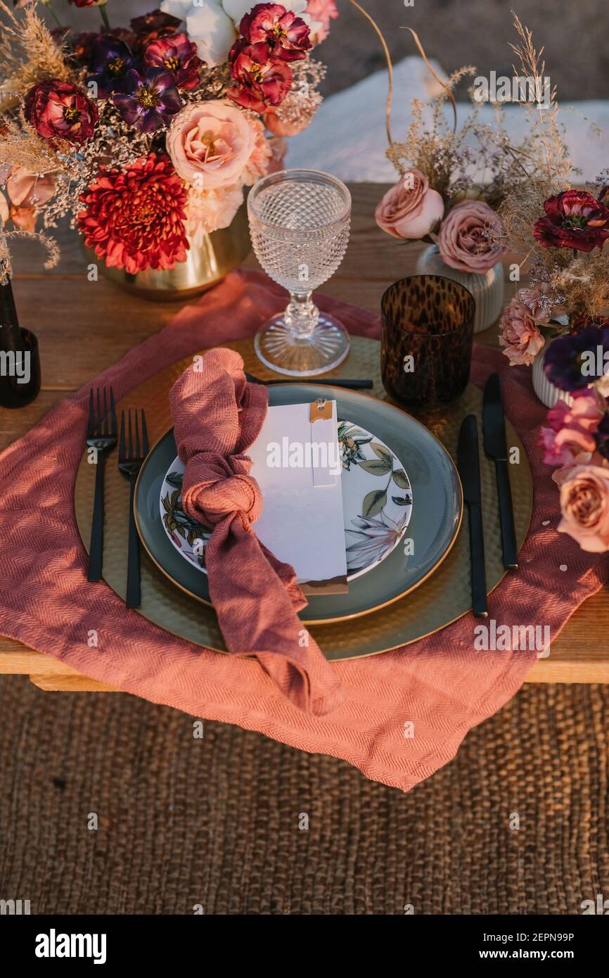 Dall'alto del tavolo di legno con posate su piatti servito su panno vicino a colorati bouquet di fiori con verricelli durante il matrimonio celebrratio Foto Stock
