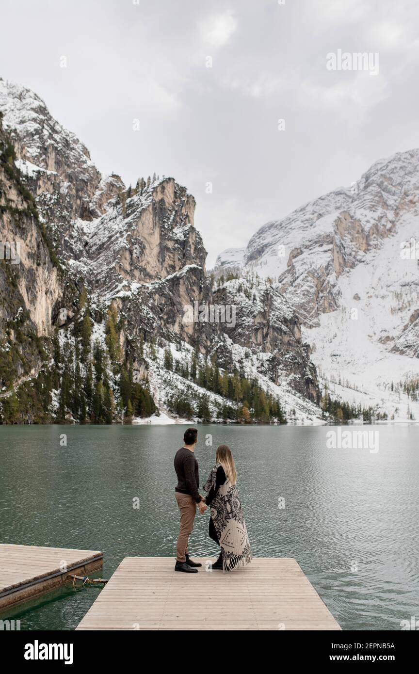 Corpo pieno di coppia dolce amorevole che si abbracciano l'un l'altro Molo in legno contro il lago di Braies circondato da neve montagne Foto Stock