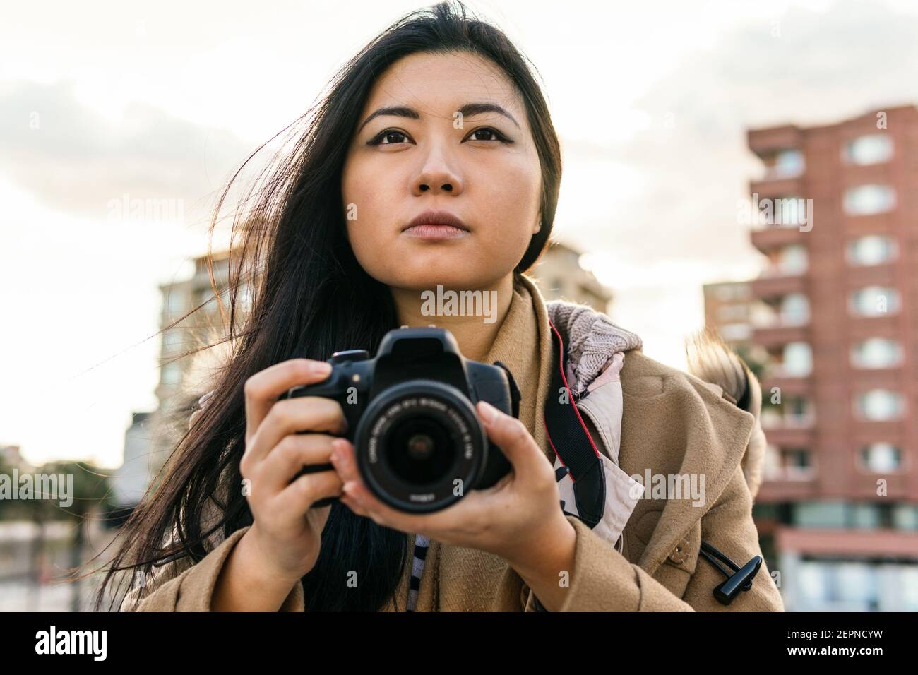 Fotografo femminile di etnia asiatica che scatta foto con una fotocamera professionale sulla strada della città Foto Stock