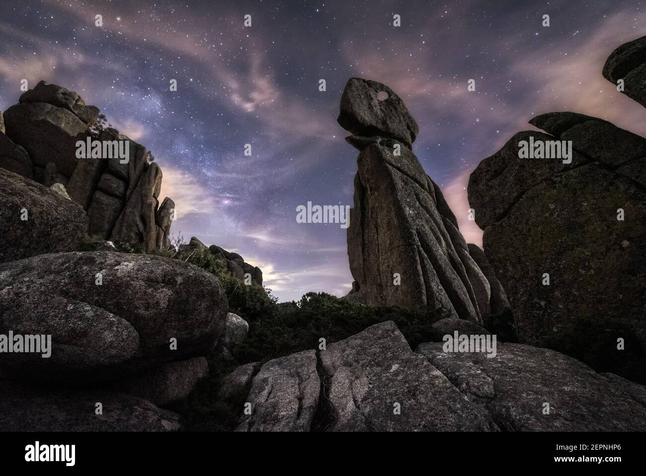 Collina con grandi rick tra piante verdi con notte colorata cielo con stelle e via lattea sullo sfondo Foto Stock