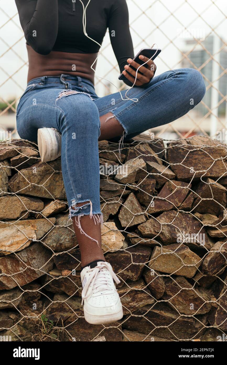 Crop nero Donna ascoltare musica con un telefono cellulare e cuffie Foto Stock
