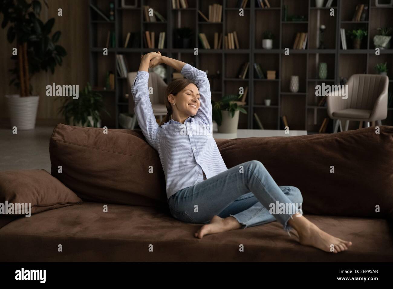 Felice giovane donna rilassarsi sul divano a casa stretching Foto Stock