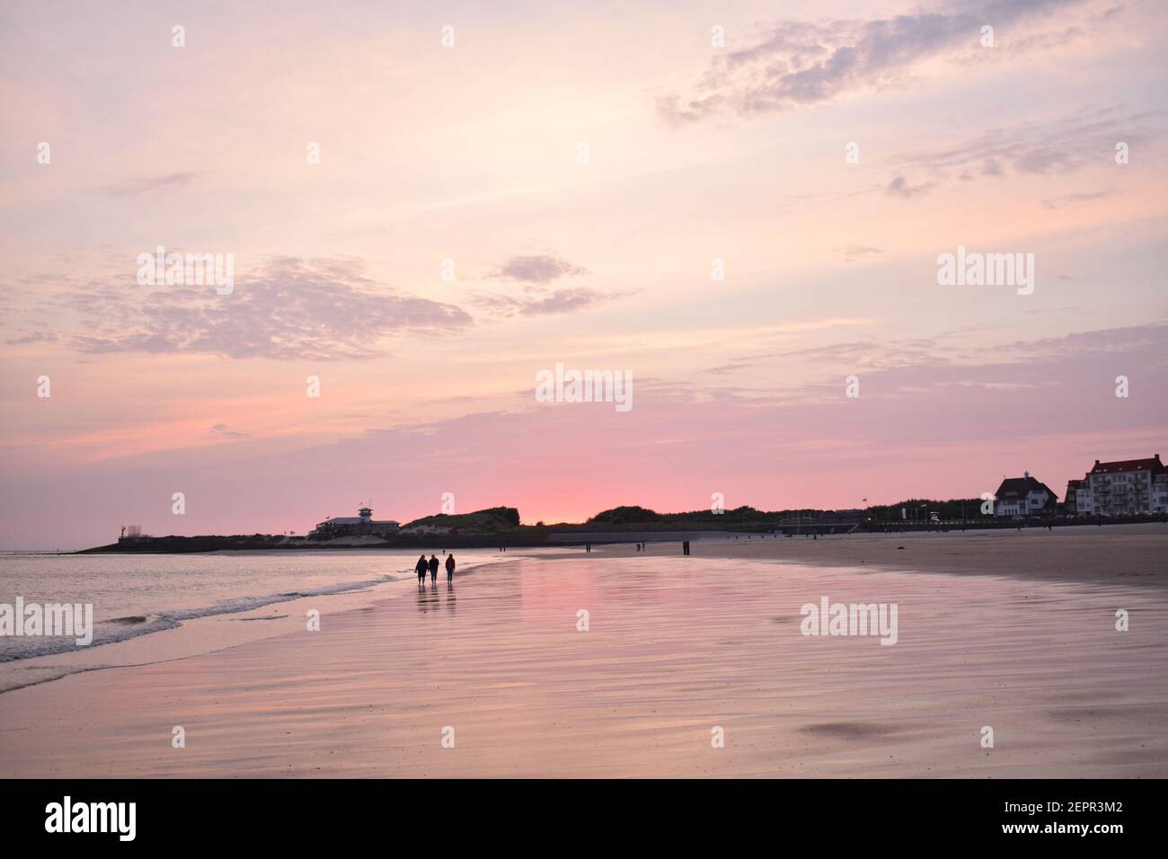 Persone che camminano sulla spiaggia olandese durante il tramonto rosa Foto Stock