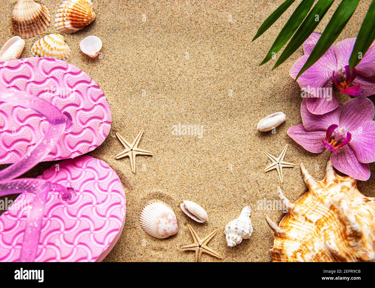 Flip Floops nella sabbia con stelle marine e fiori di orchidee. In estate sulla spiaggia. Spiaggia estiva. Foto Stock