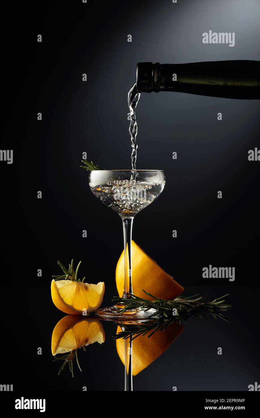 Il gin viene versato in un piccolo bicchiere di un'antica bottiglia di  vetro scuro. Una bevanda alcolica forte con limone e rosmarino su sfondo  nero riflettente Foto stock - Alamy