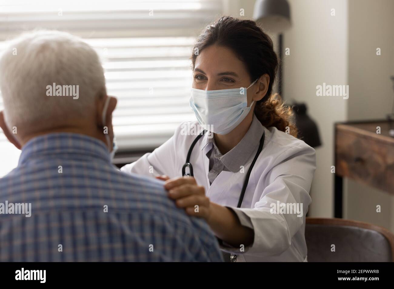 Primo piano medico donna che indossa una maschera che tocca la spalla del paziente anziano Foto Stock