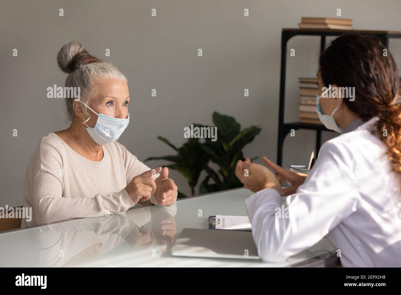 Primo piano donna matura indossando maschera di faccia ascoltando il medico Foto Stock