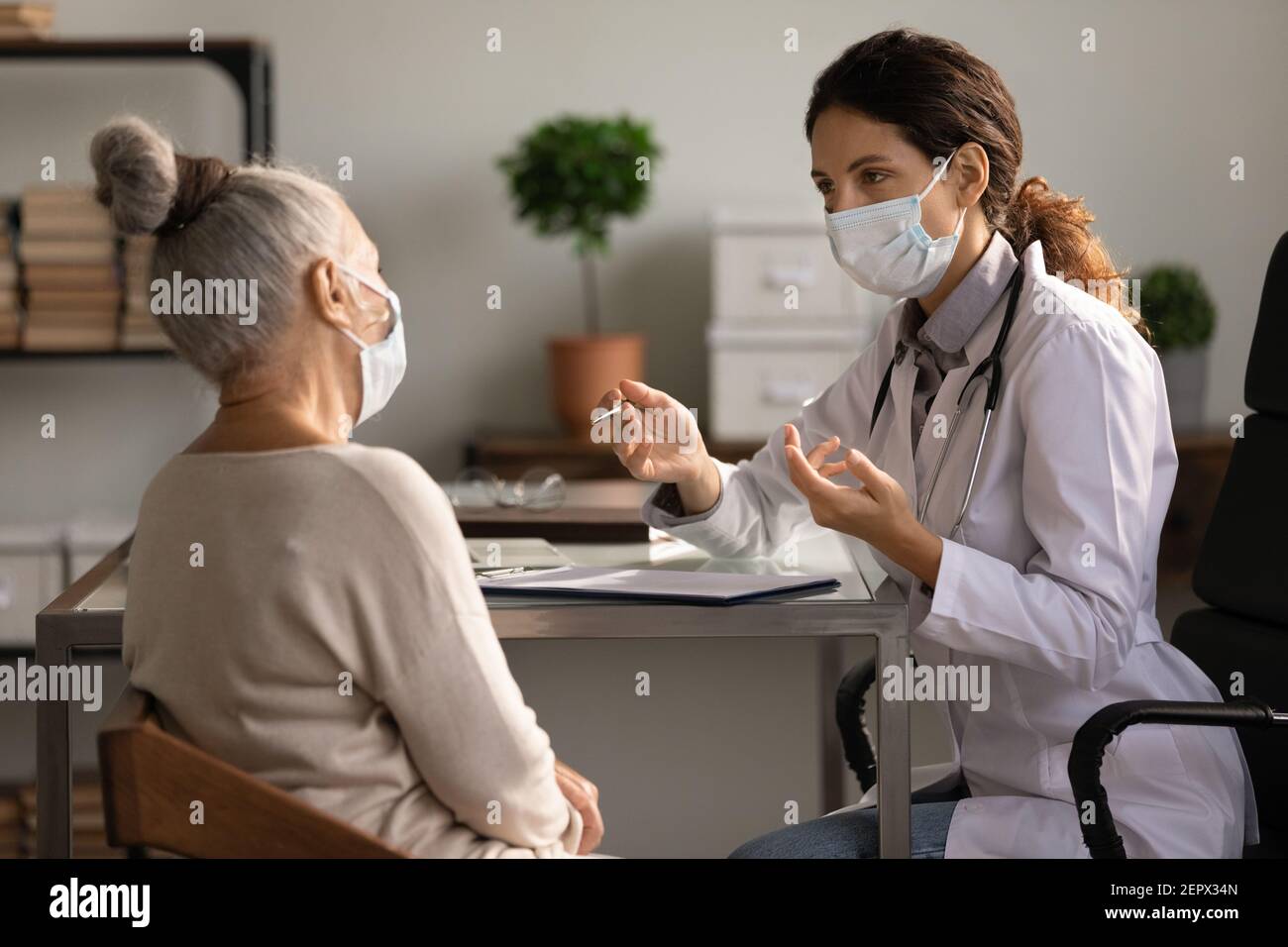 Primo piano medico serio che indossa maschera consultando paziente donna matura Foto Stock