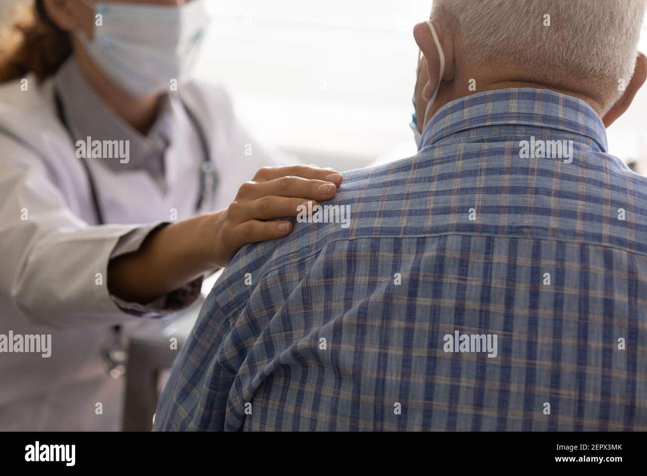 Primo piano medico indossando maschera confortante paziente maturo, toccando spalla Foto Stock