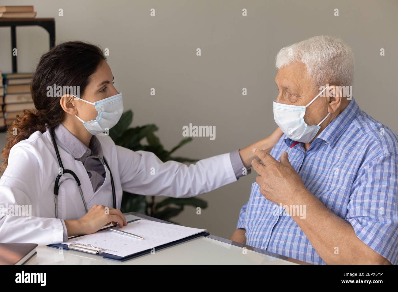 Vista laterale medico donna che cura indossando maschera che conforta paziente maturo Foto Stock