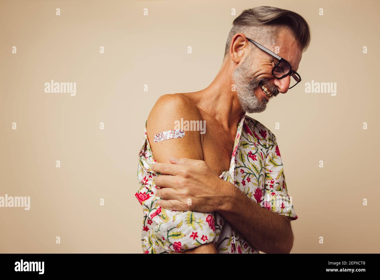 Uomo bearded sorridente con bendaggio sul braccio dopo aver ricevuto il vaccino di immunità. Uomo maturo che si è rilassato dopo aver ricevuto il vaccino covid-19. Foto Stock