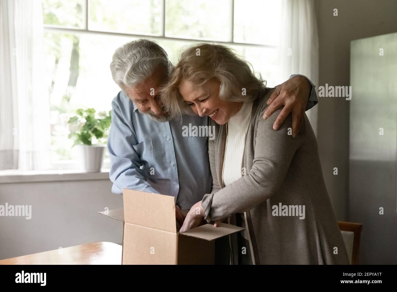 Felice eccitato coppia matura famiglia disimballaggio pacco a casa Foto Stock