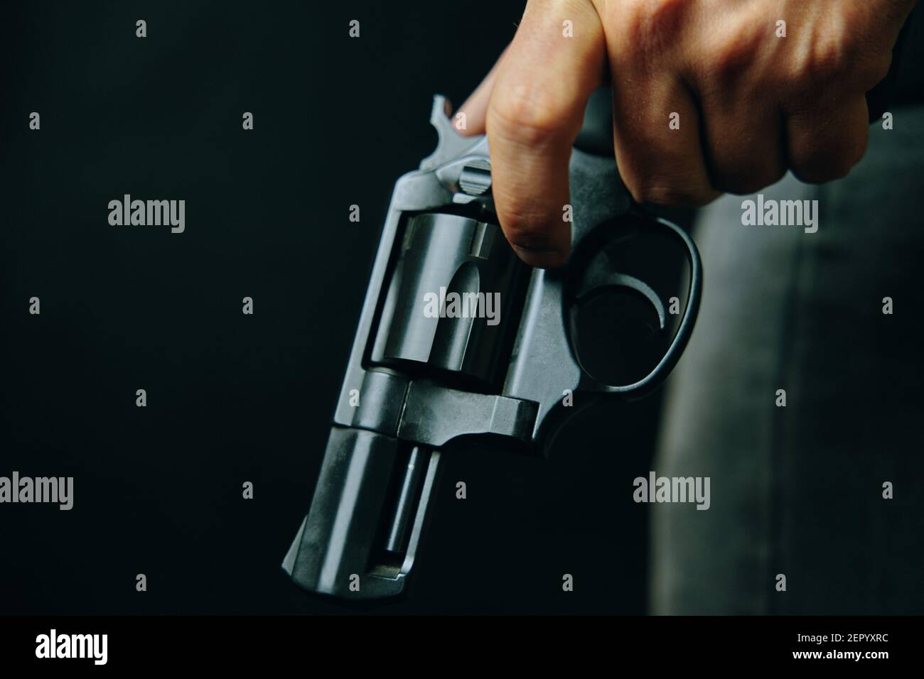Arma da fuoco in mano dell'uomo. Criminale con rivoltatore su sfondo scuro. Pistola abbassata con tamburo. Difesa o attacco. Assassino o ladro armato. Foto Stock