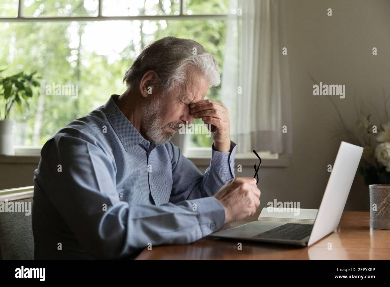 Stanco uomo degli anni '60 che lavora in un notebook da casa Foto Stock