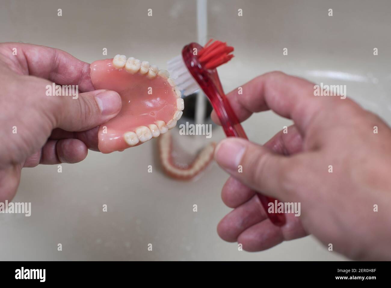 Dentiera di pulizia con spazzola nel lavandino con acqua corrente Foto Stock