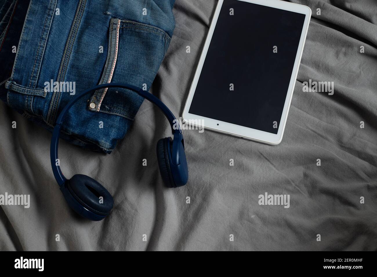 jeans da uomo sul letto accanto a cuffie e tablet Foto Stock