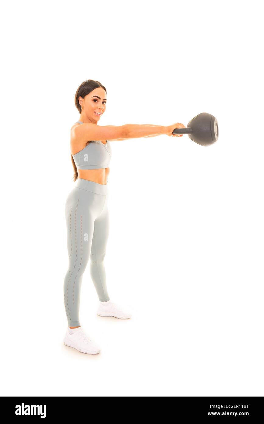 Ritratto verticale di una giovane donna che solleva un kettlebell di 15 kg mentre si fa un allenamento, isolato su uno sfondo bianco. Foto Stock