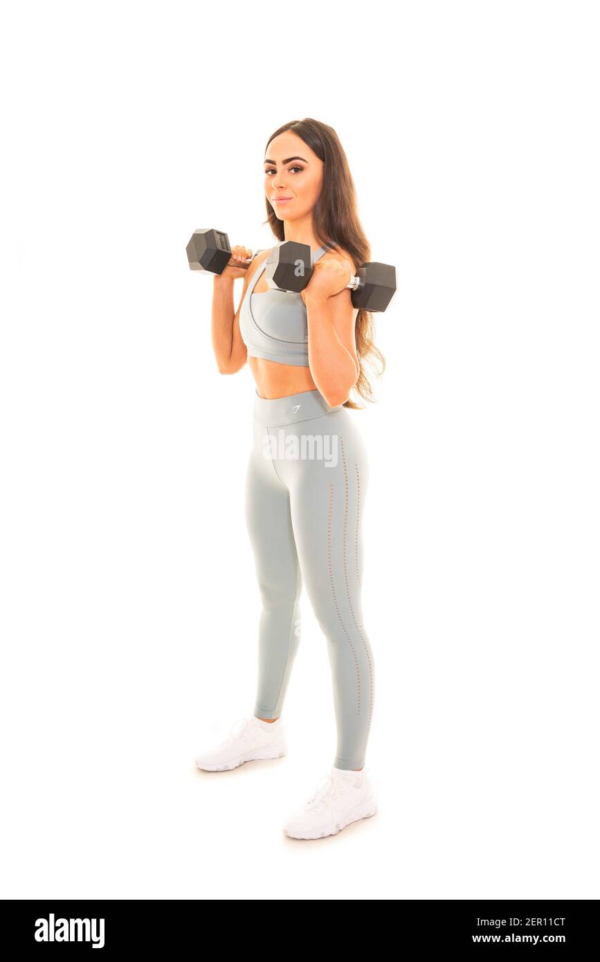 Ritratto verticale di una giovane donna che usa i manubri in un allenamento, isolato su uno sfondo bianco. Foto Stock
