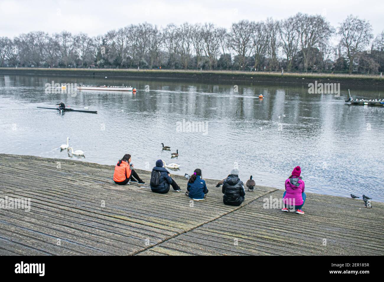 PUTNEY LONDON, REGNO UNITO 28 FEBBRAIO 2021. Un vogatore passa davanti a un gruppo di persone che si siedono sulla riva del fiume a Putney in una giornata più fredda a Londra dopo le calde temperature del giorno prima. Credit amer Ghazzal/Alamy Live News Foto Stock