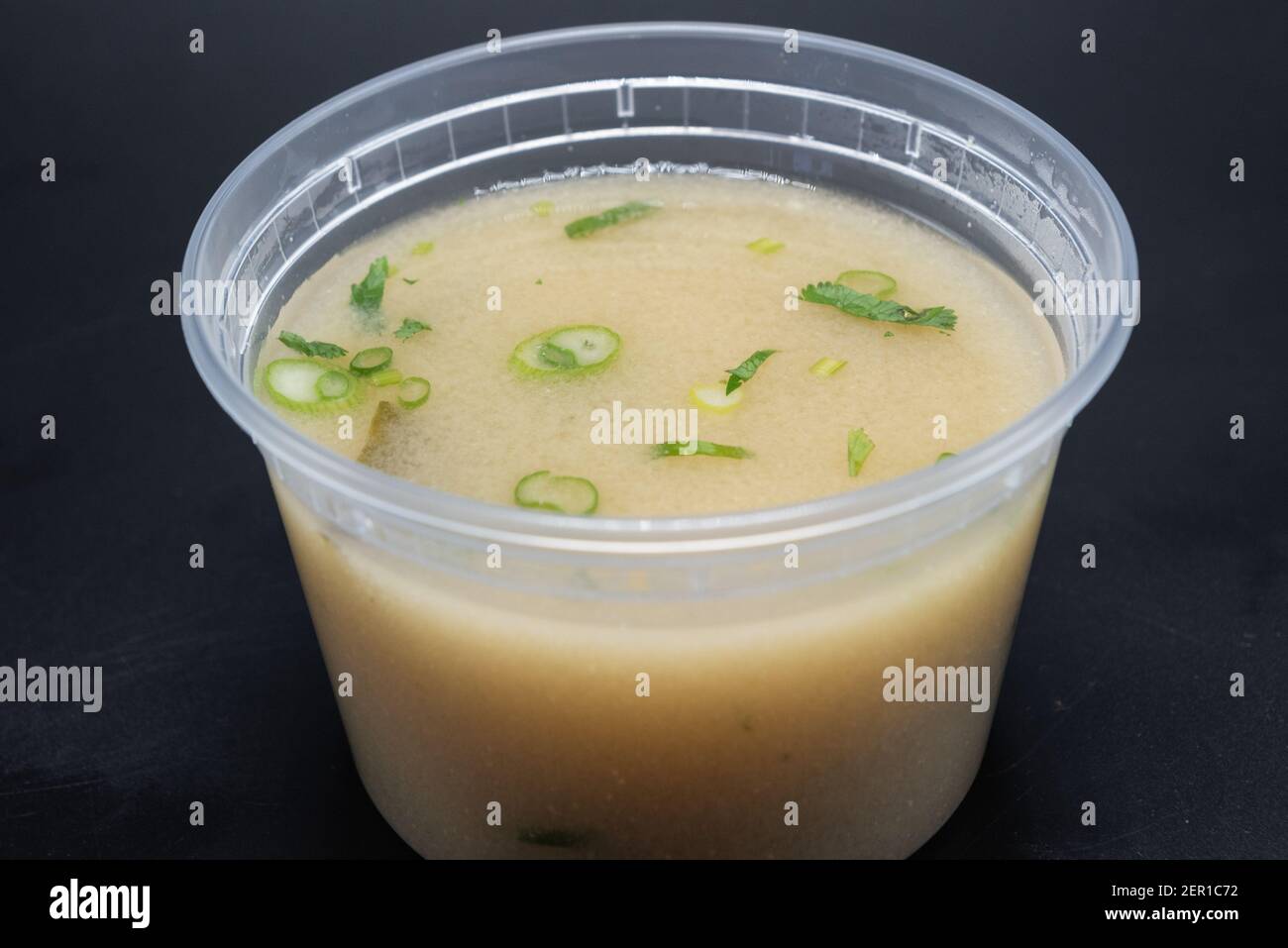 La ciotola della zuppa di Miso mostra un delizioso brodo torbido contenente cipolla verde, alghe e sapore speziato in un contenitore trasparente. Foto Stock