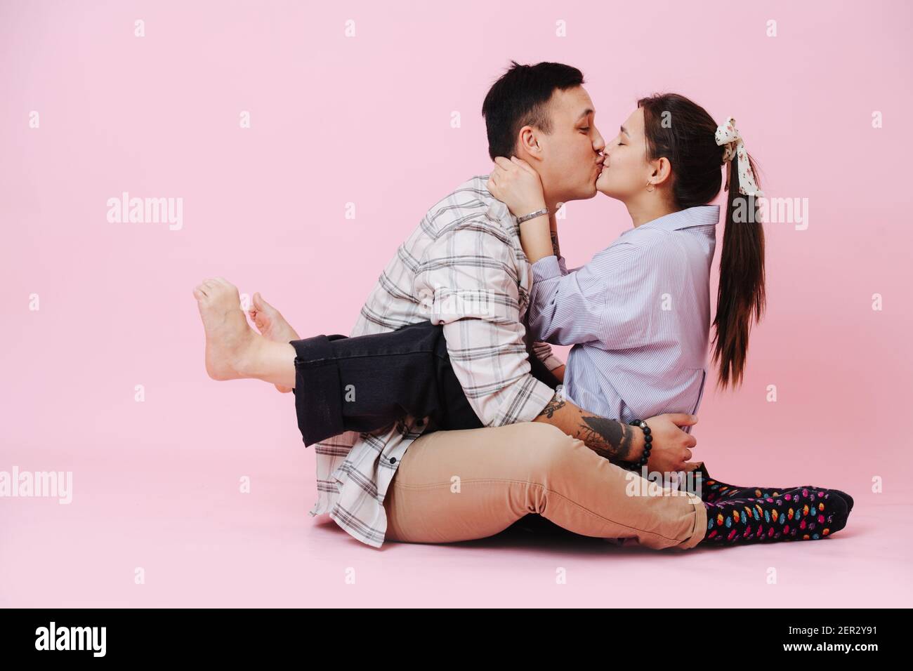 Giovane coppia abbracciando e baciando su sfondo rosa, la ragazza si siede sul ragazzo Foto Stock
