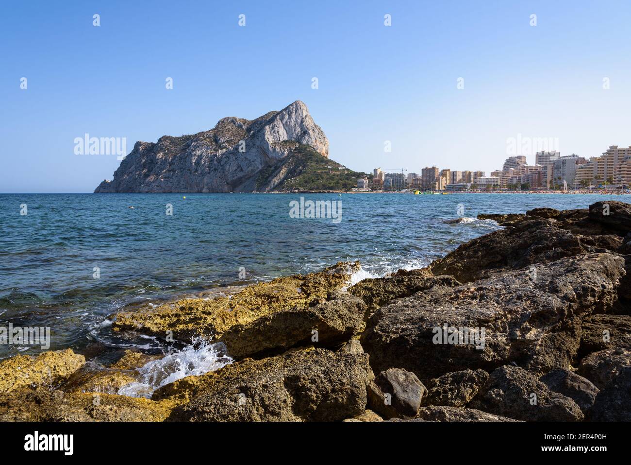 Vista dalle rocce della costa con la spiaggia urbana di Calpe e la falesia sullo sfondo, Alicante, Spagna Foto Stock