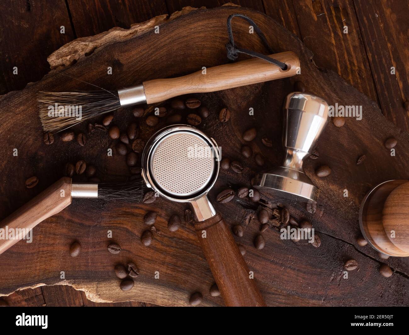 Utensili da caffè barista (manomissione, livellatore di distribuzione, spazzole) e chicchi di caffè tostati su tavola di legno Foto Stock