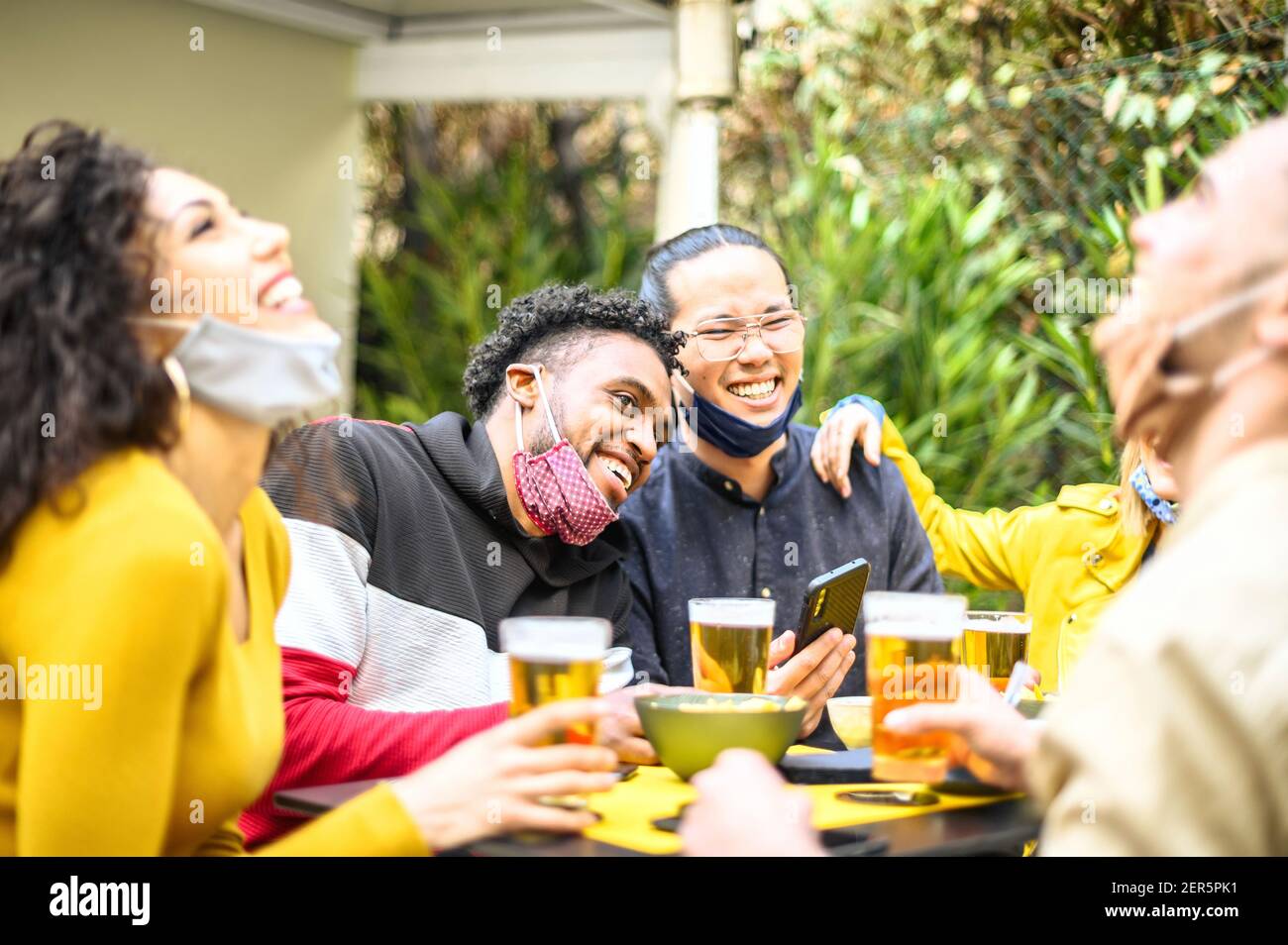 Persone multirazziali sorridenti con maschera aperta in giardino Del ristorante mentre beve birra - nuovo concetto di stile di vita normale su havi amici felici Foto Stock