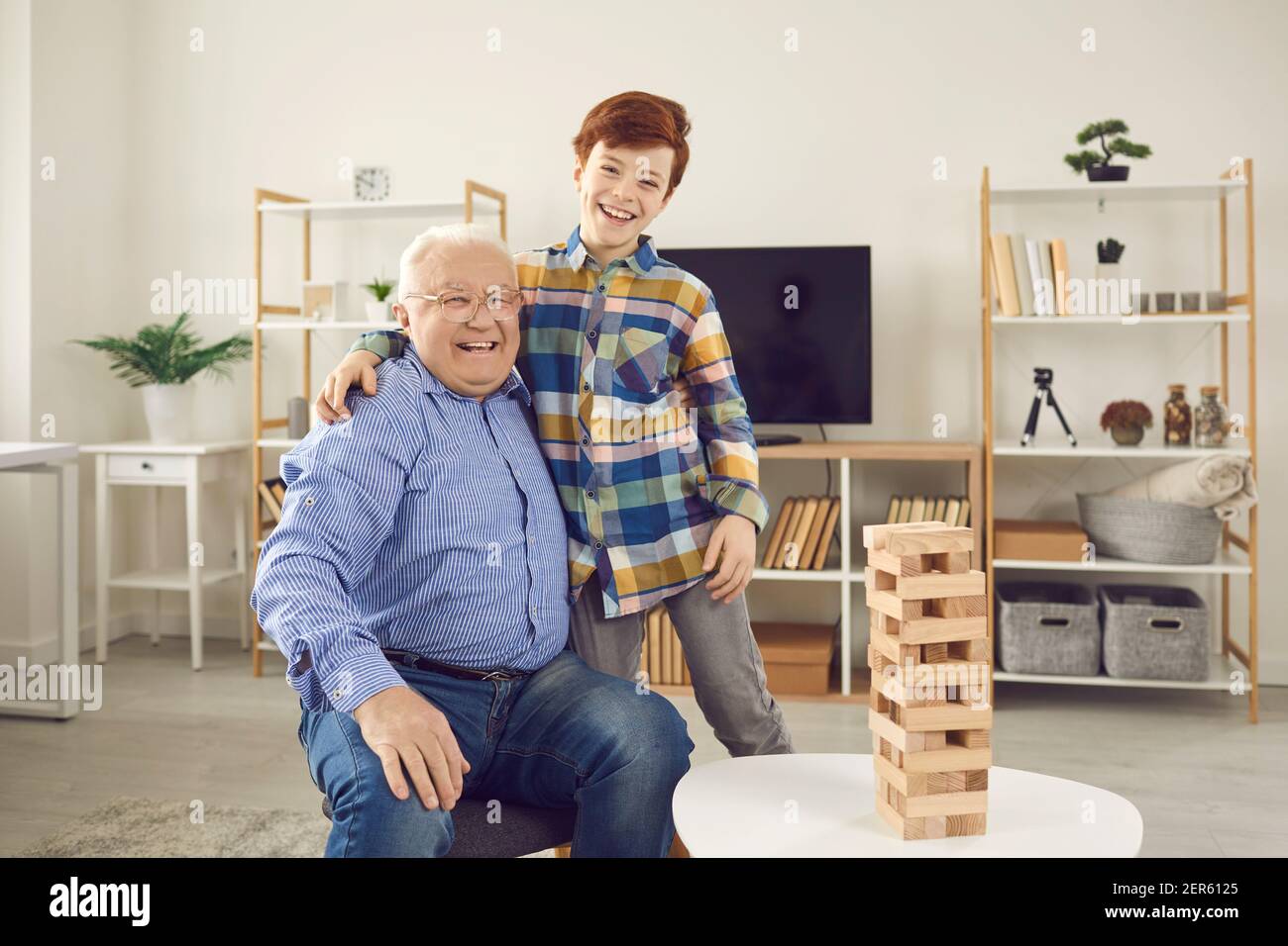 Felice sorridendo il vecchio nonno e il suo nipote positivo che abbracciava a casa guardando la fotocamera Foto Stock