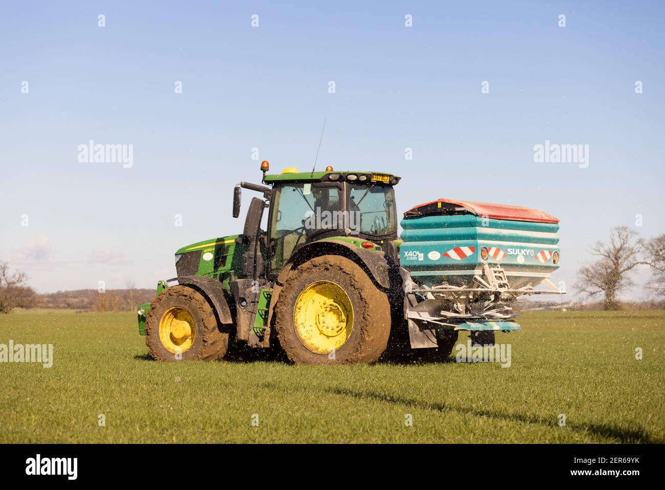 Coltivatore che guida trattore e fertilizzante spruzzante in un campo all'inizio della primavera 2021. Hertfordshire Regno Unito Foto Stock