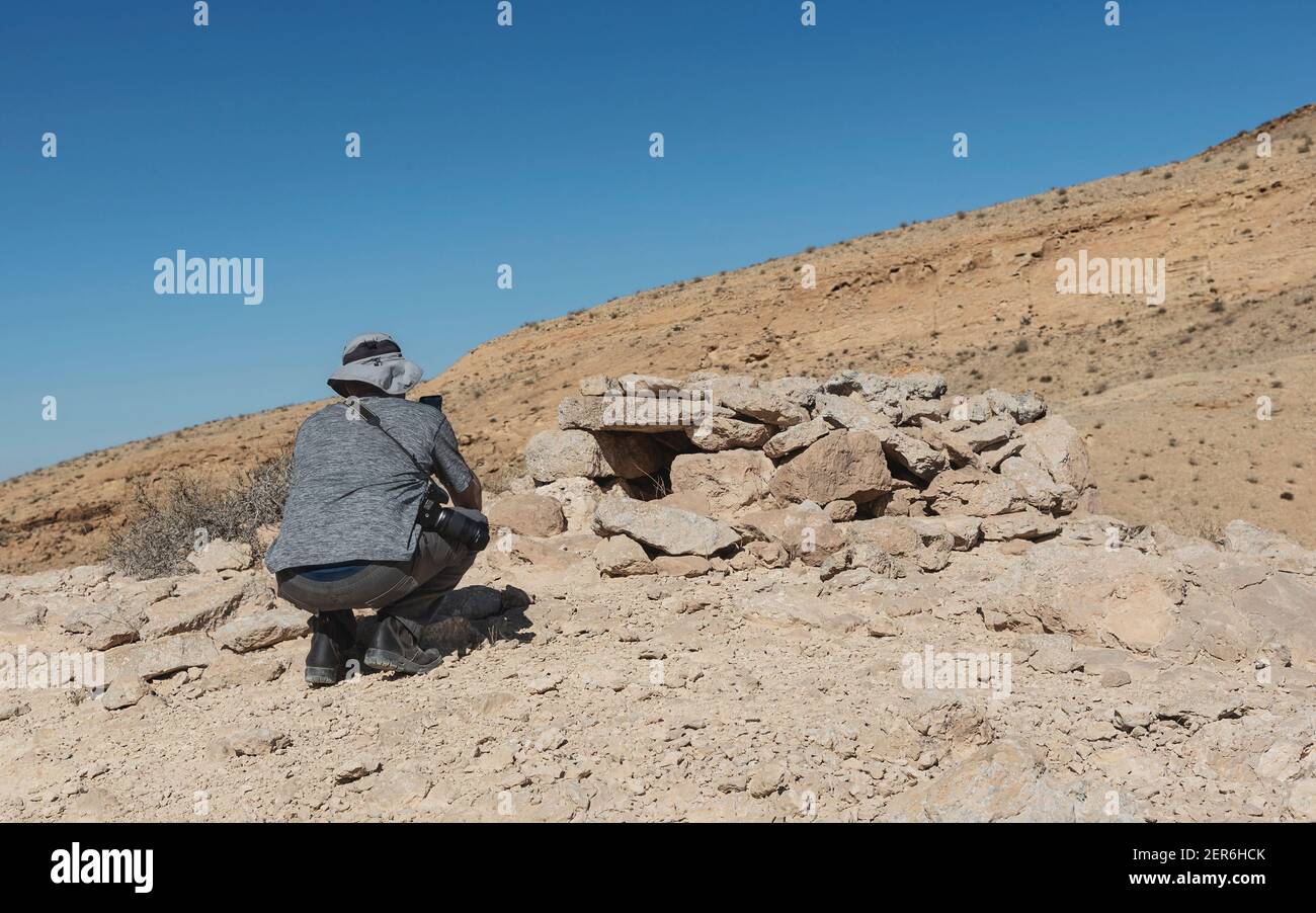 una persona che scatta foto di un antico animale beduino in pietra Trappola per leopardi vicino al cratere Makhtesh Ramon in Israele con un backgroun cielo blu chiaro Foto Stock