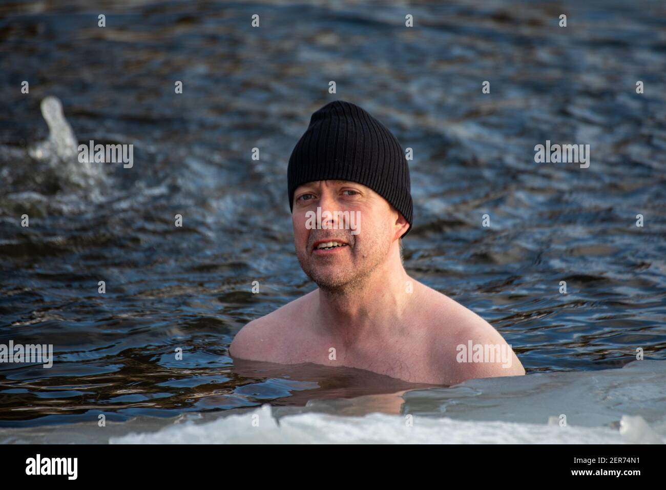 Uomo che indossa una beania durante il nuoto invernale in una buca per il ghiaccio o avanto nel distretto di Munkkiniemi di Helsinki, Finlandia Foto Stock