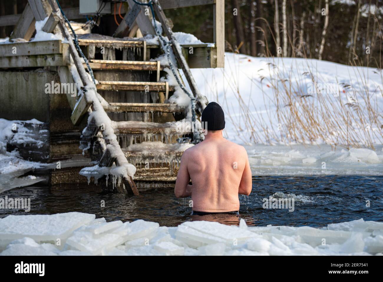 Uomo in piedi in avanto o buca per nuotare sul ghiaccio dopo il nuoto invernale nel distretto di Munkkiniemi di Helsinki, Finlandia Foto Stock