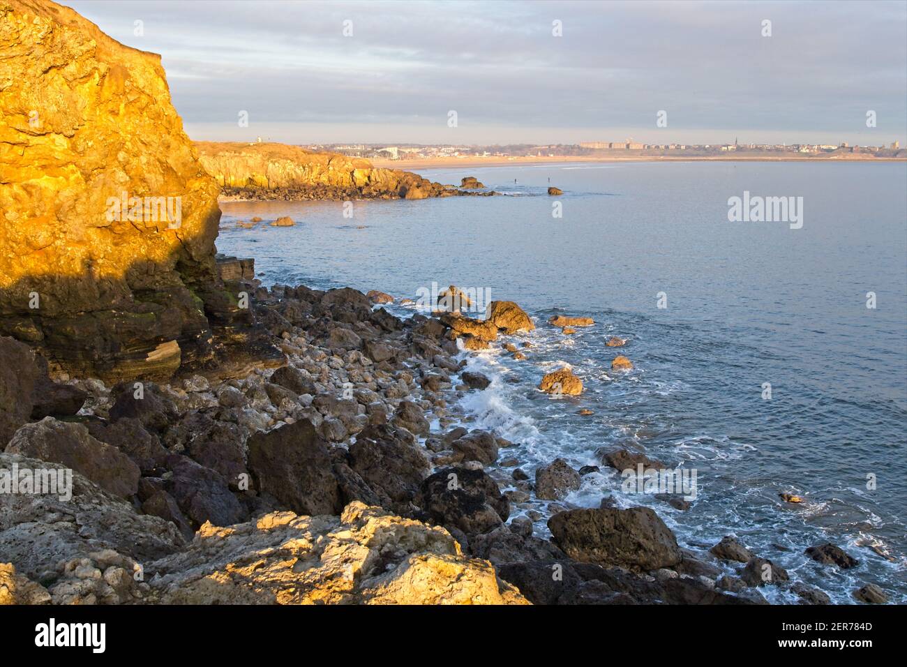 La luce del sole dorata del mattino presto illumina le scogliere e gli affioramenti calcarei a Trow Rocks sulla costa del Mare del Nord a South Shields in Tyne and Wear. Foto Stock