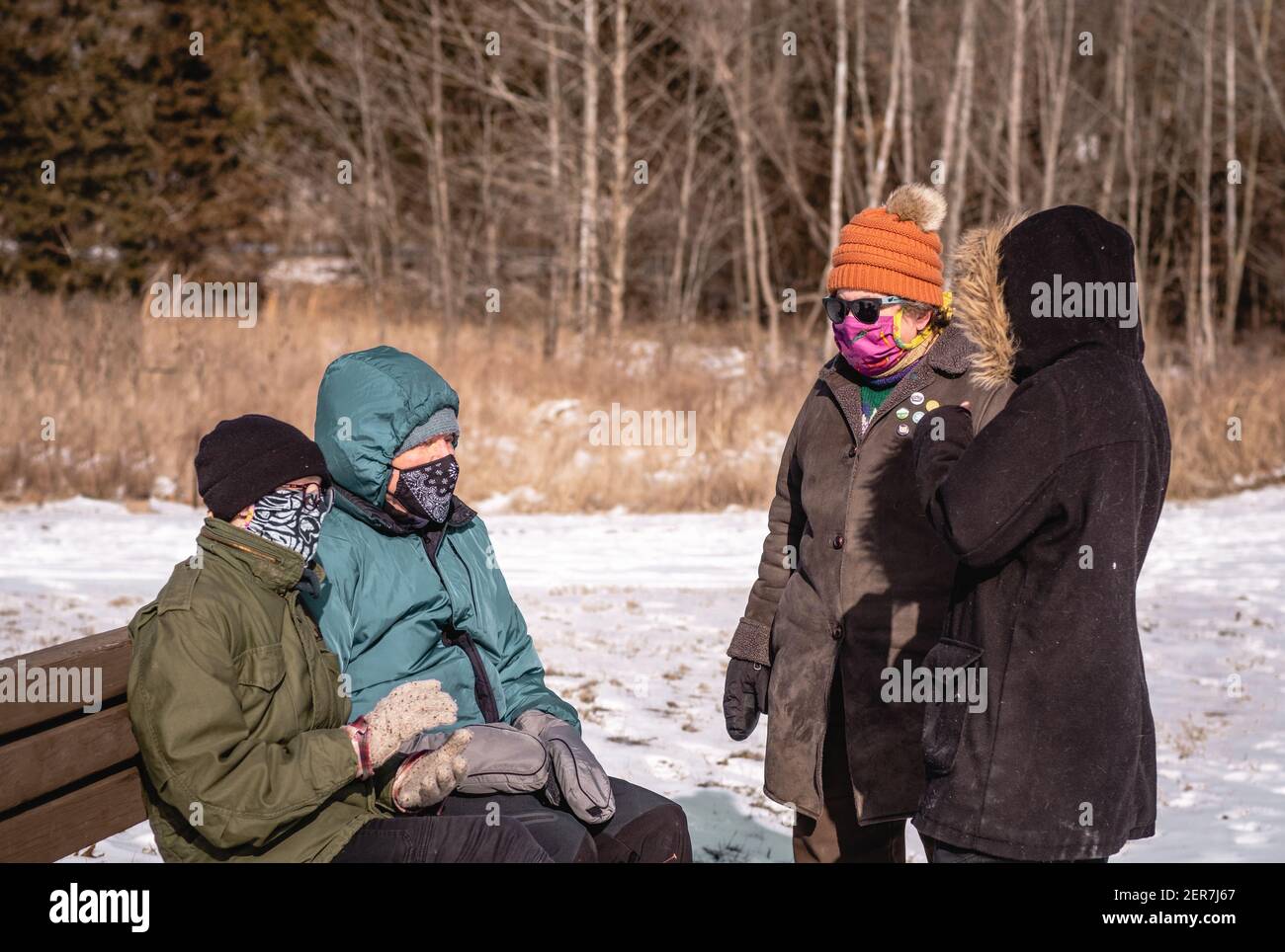 Vista del nonno, della sua figlia di mezza età in visita e di due giovani nipoti adulti che parlano all'aperto mentre indossano maschere protettive sul col Foto Stock