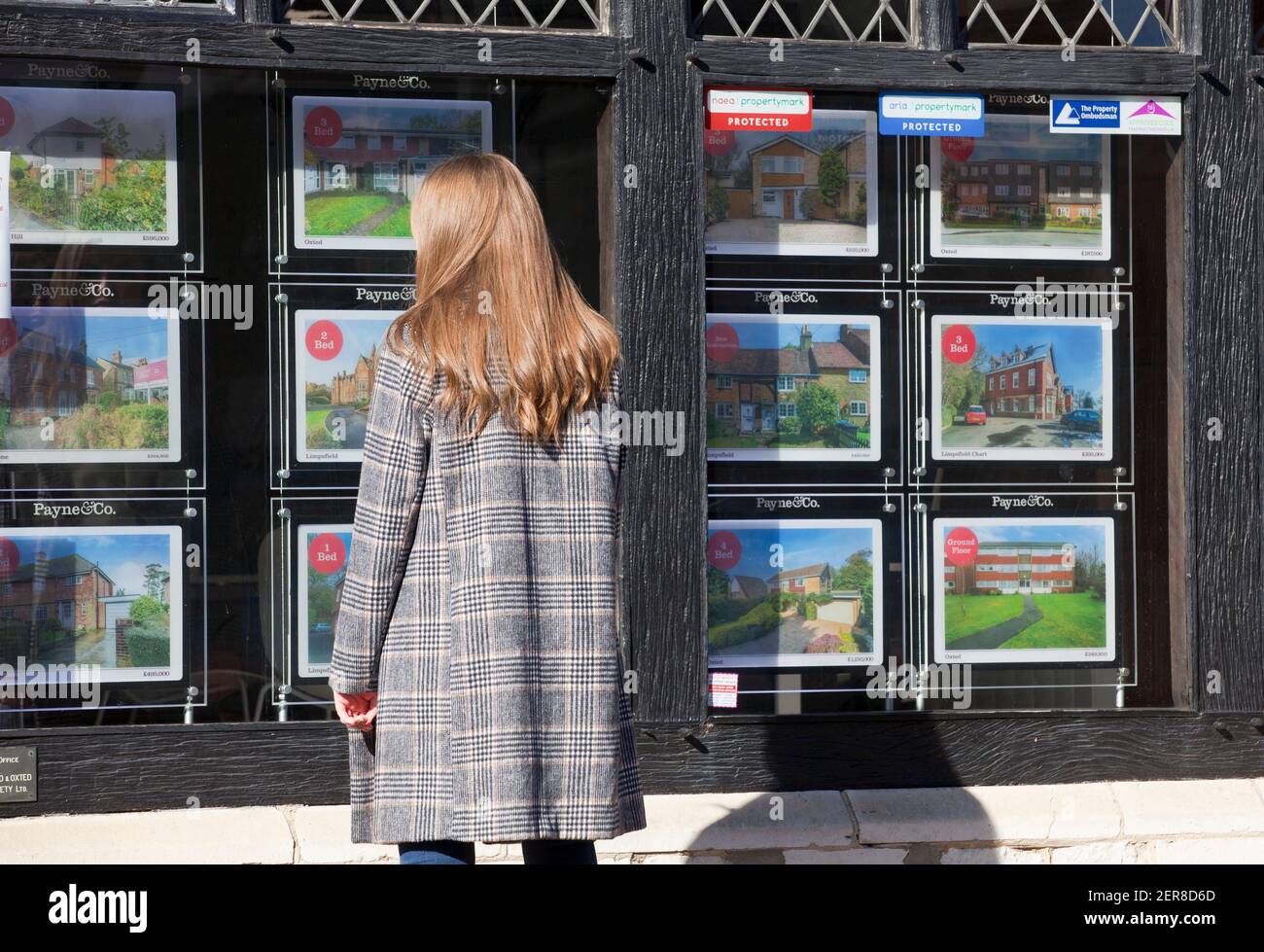 Una giovane donna ( modello rilasciato ) che guarda in una finestra di un agente immobiliare a Surrey, Inghilterra, Regno Unito. Febbraio 2021 Foto Stock
