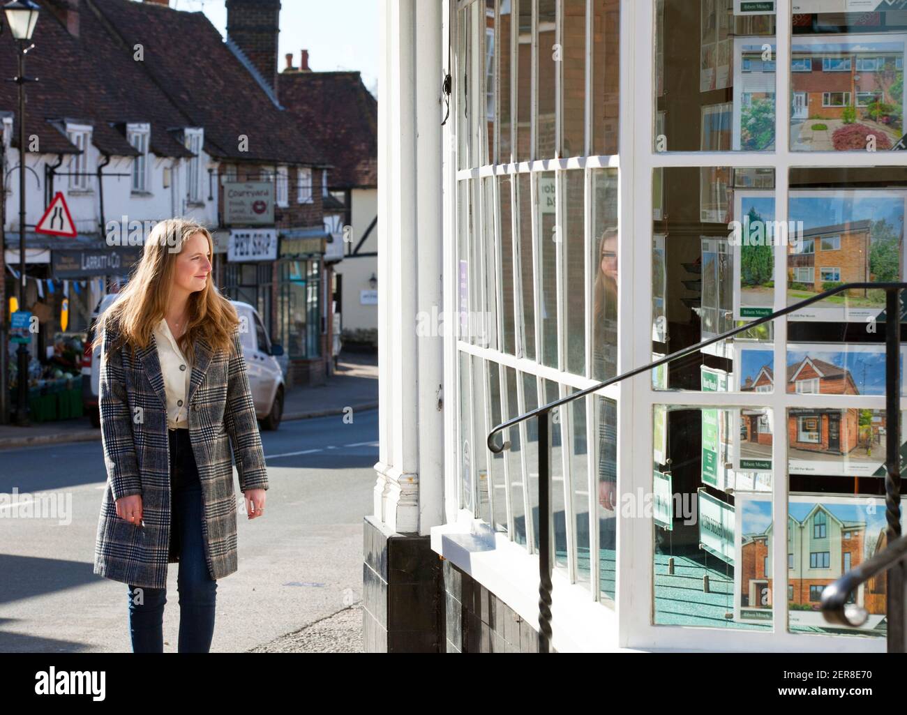 Una giovane donna ( modello rilasciato ) che guarda in una finestra di un agente immobiliare a Westerham, Kent, Inghilterra, Regno Unito. Febbraio 2021 Foto Stock