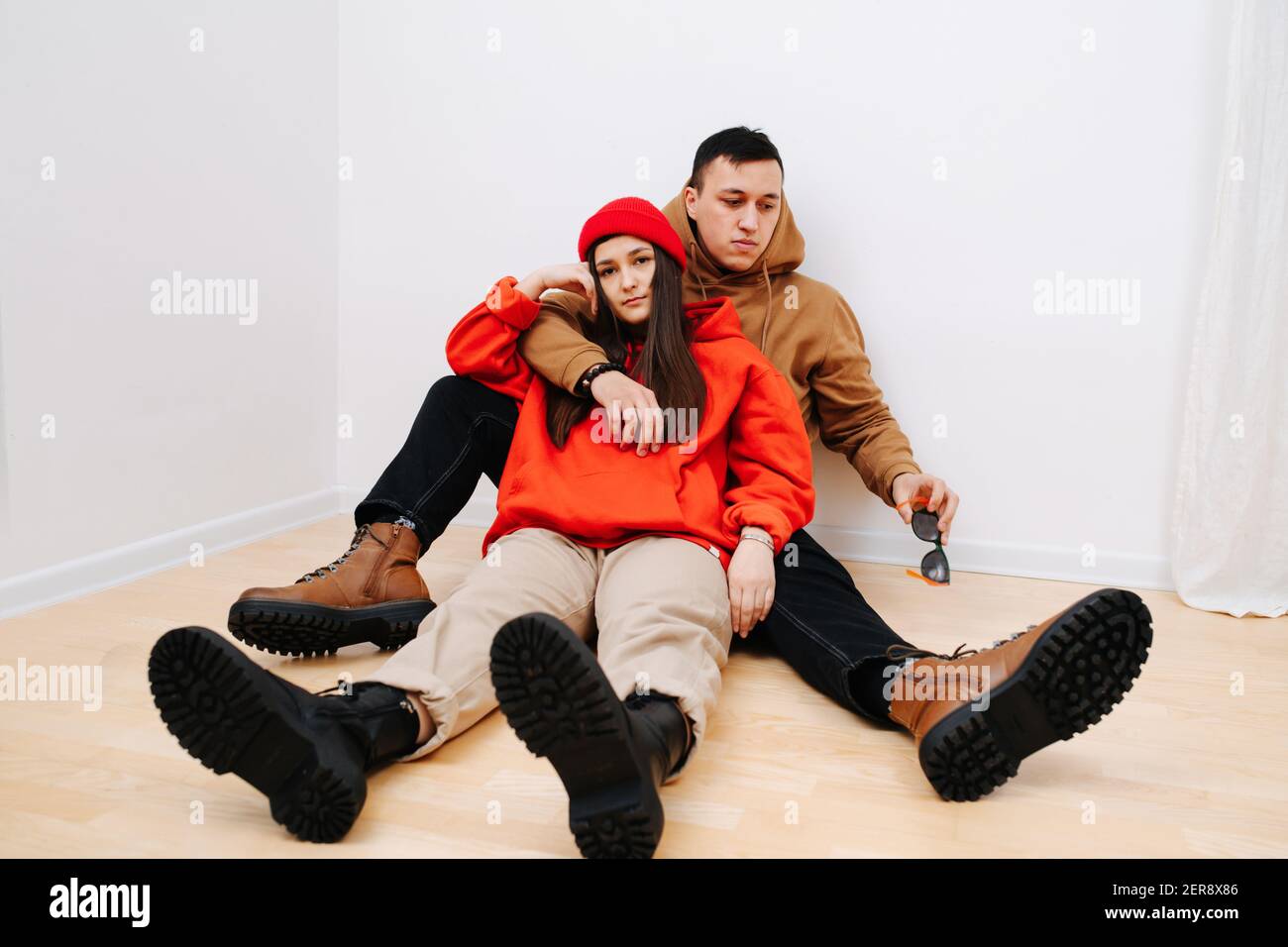 Giovane uomo e donna si coccolano, seduti a terra in felpe e stivali militari Foto Stock