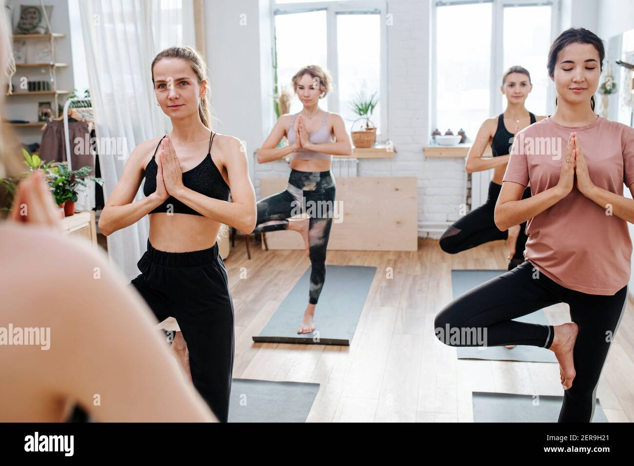 Donne felici che praticano lo yoga di fronte all'istruttore, bilanciandosi su un piede Foto Stock