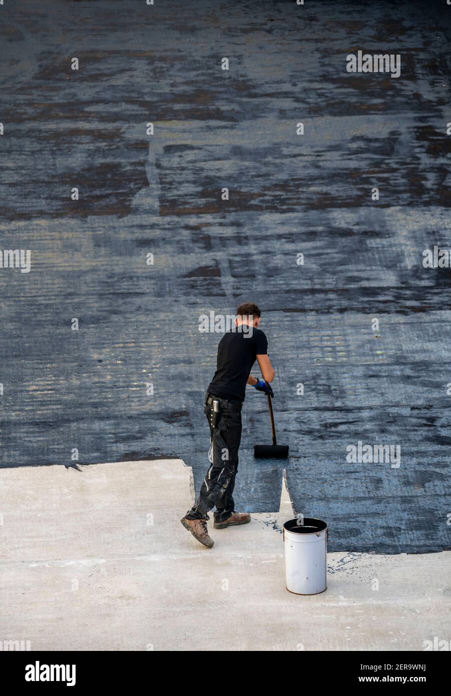 Cantiere, applicazione di un rivestimento bituminoso su un soffitto in calcestruzzo, preparazione per impermeabilizzazione, con telatura bituminosa applicata al centro Foto Stock