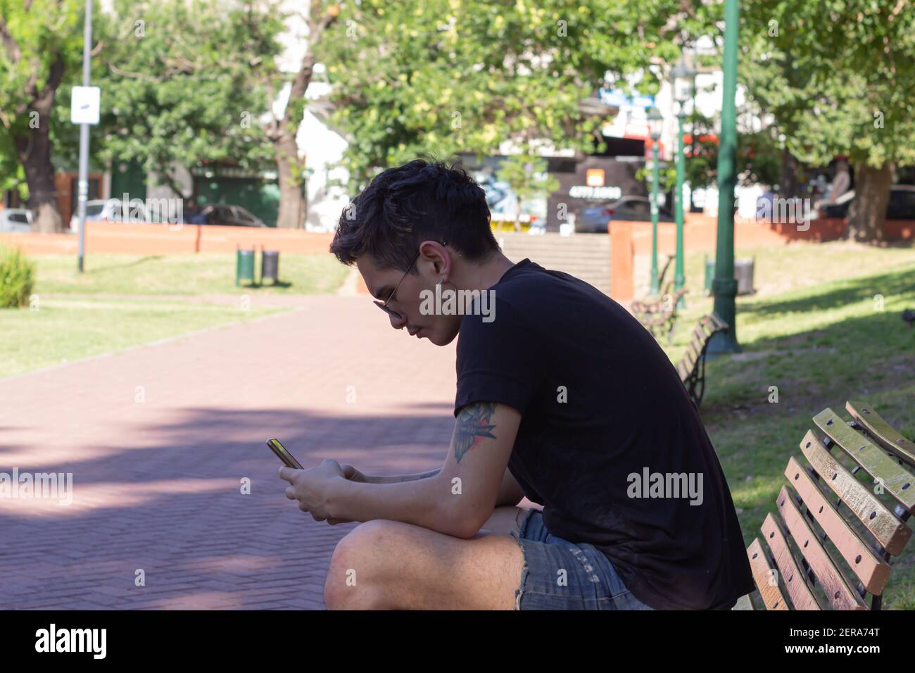 Giovane uomo che invia un messaggio di testo seduto su una panchina in una giornata di sole. Foto Stock
