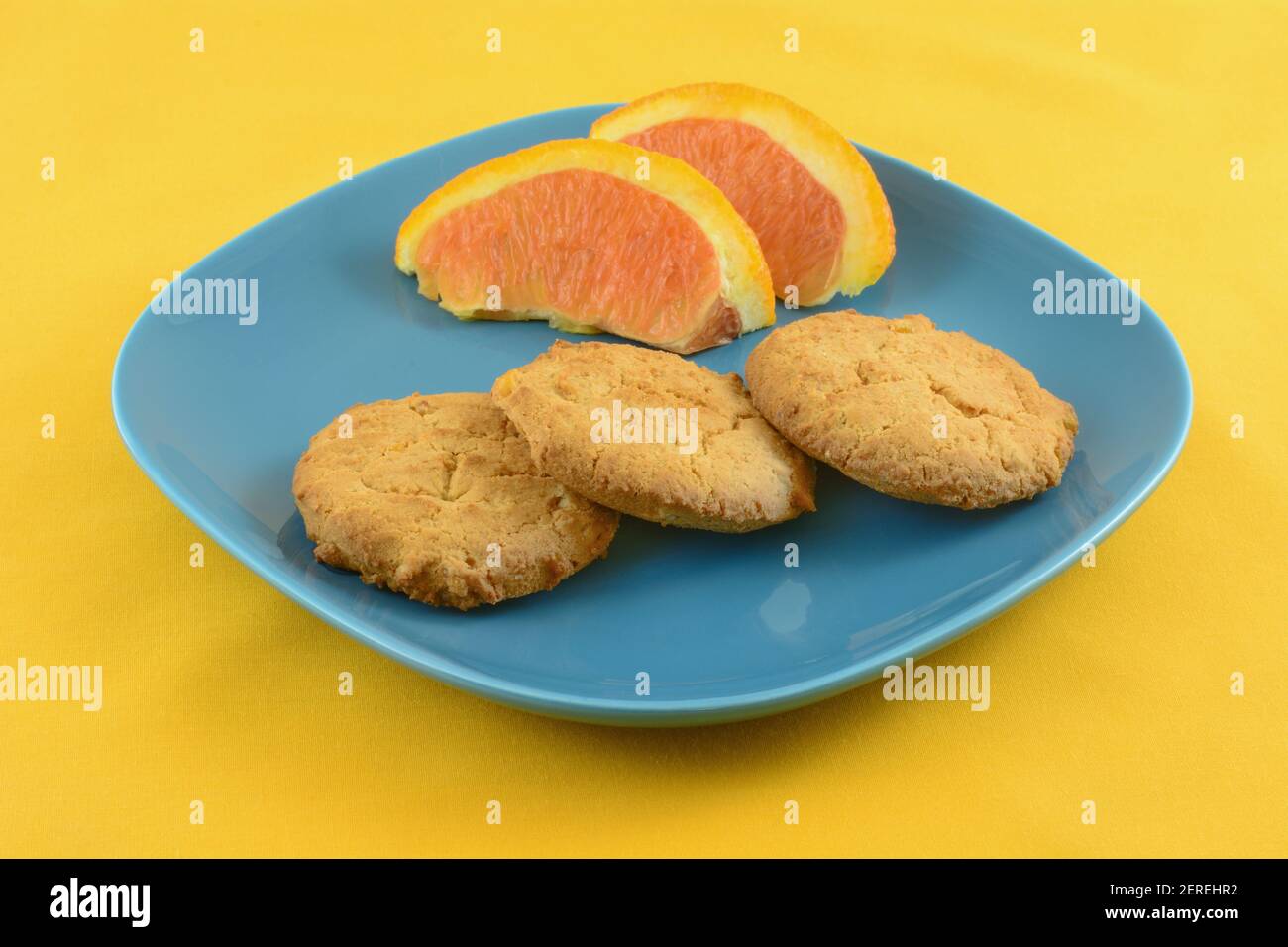 Biscotti al burro di scorza d'arancia con fette d'arancia su spuntino blu piatto su tovaglia gialla Foto Stock