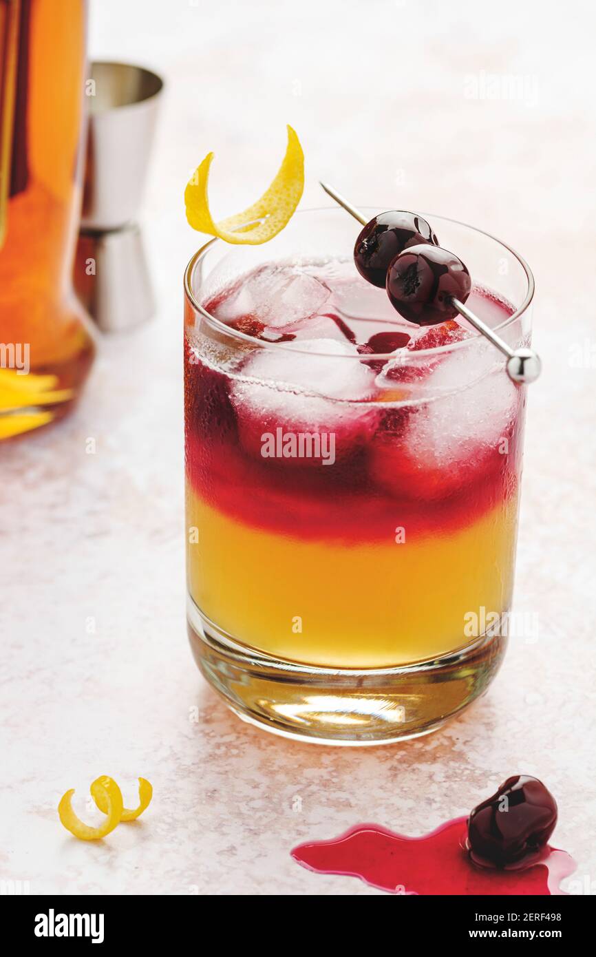 New York Whiskey si affina in un bicchiere con cubetti di ghiaccio, ciliegie in cima con sciroppo e scorze di limone. Foto Stock